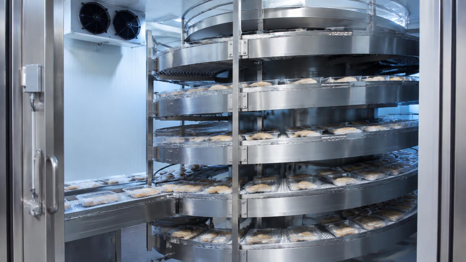 Spiral freezer conveyor carrying food products through a cold insulated enclosure